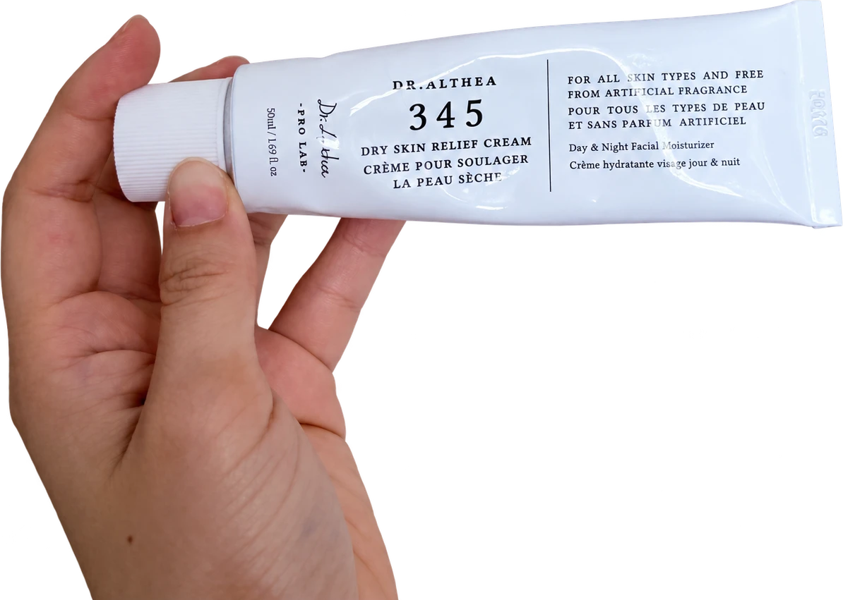 A hand holding a creased white Dr. Althea 345 cream tube with its cap on the left.