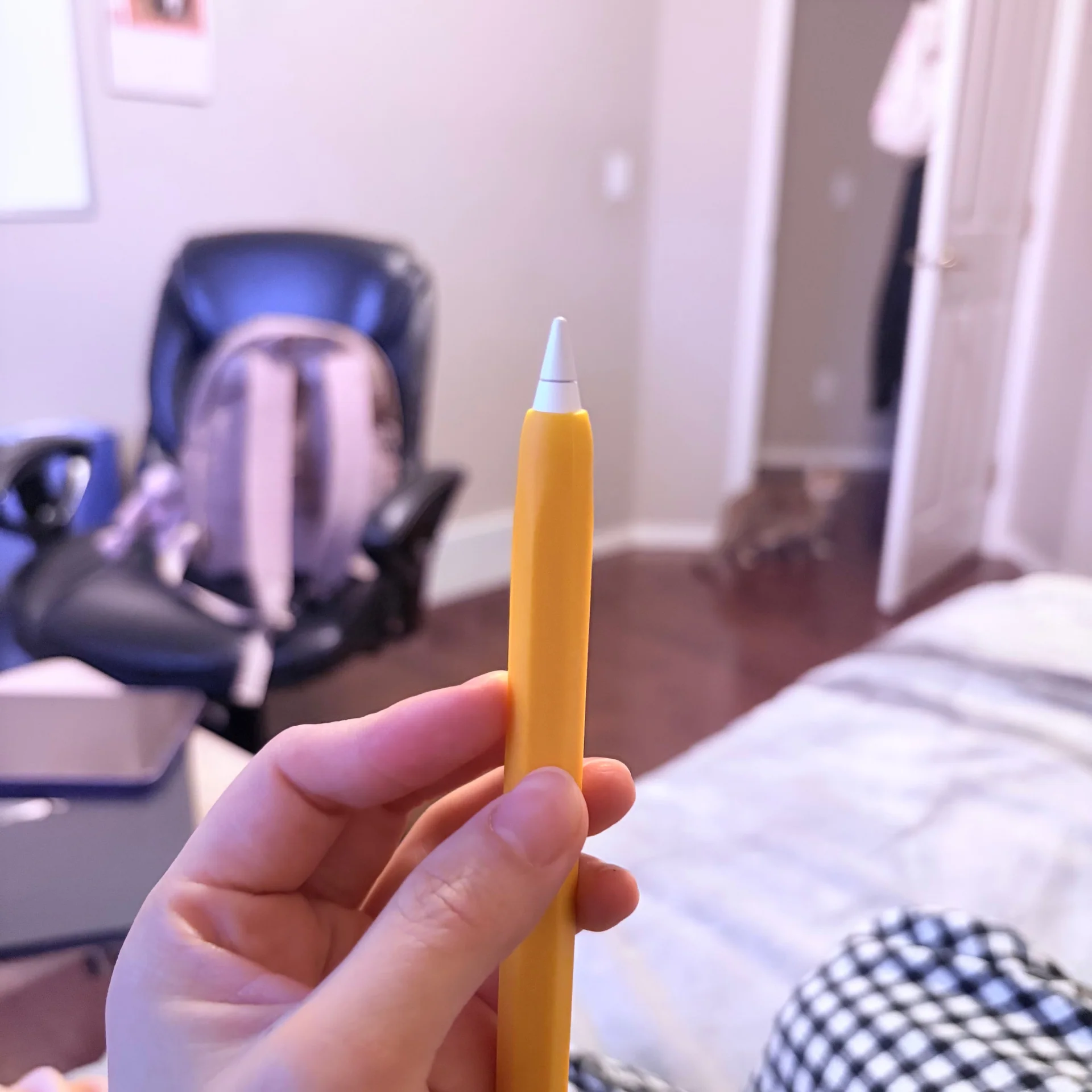 A hand holding an Apple Pencil fitted with a yellow silicone grip.